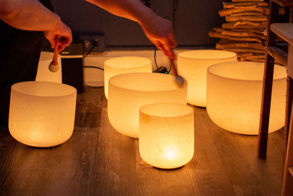 Hands playing with resonance bowls that are lit with candles emitting a yellow glow.