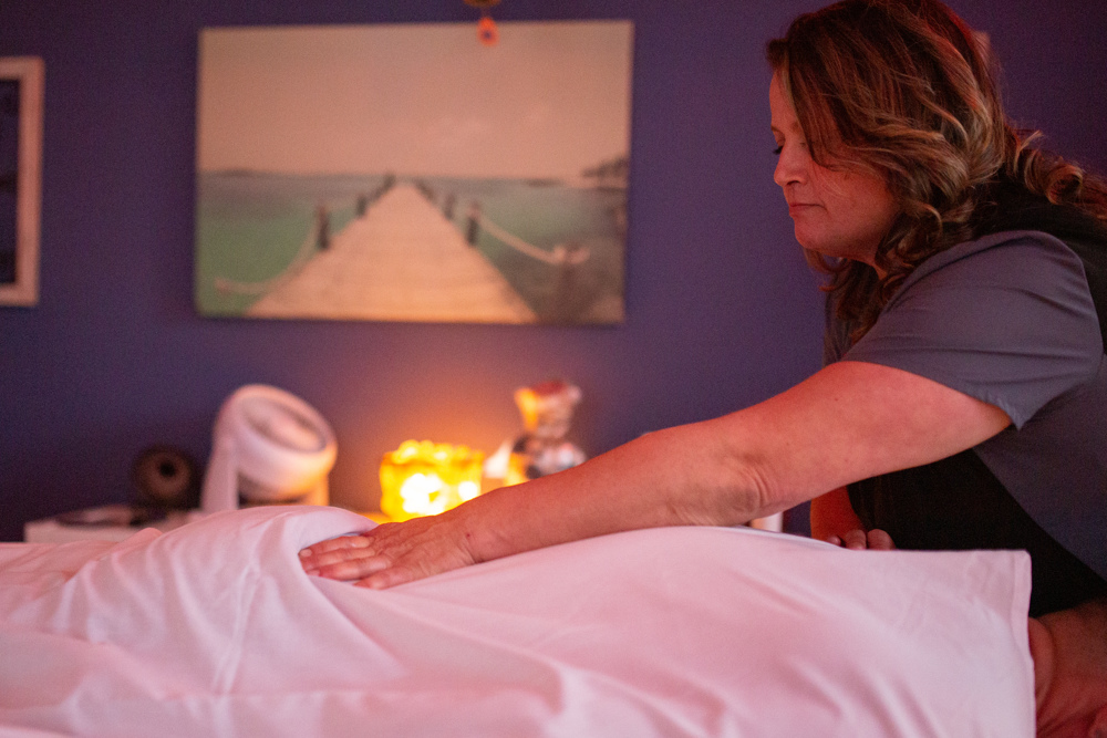 Woman massaging person's lower back on massage table in a dim lit room at Jardin's Magical Hands in Sacramento, CA